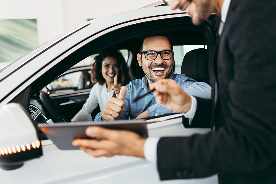 a couple in a car interacting with a salesman